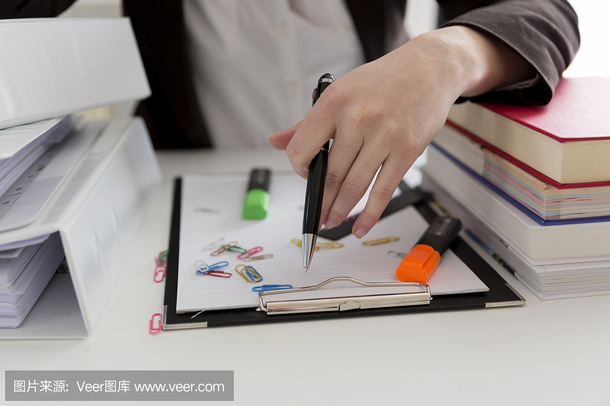 坐在滿是文書,書籍和文件的桌子旁的女人。混亂的工作場所。過載和過度勞累